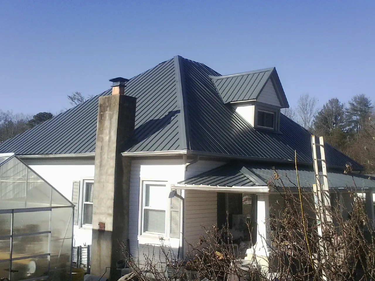 Dark blue standing seam metal roof on a white farmhouse with dormer — Slate & Tile Roof Repair by Roofing Brothers in Orangeburg